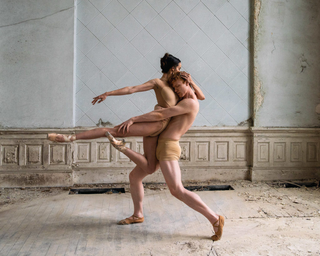 Two ballet dancers hold a posed embrace.