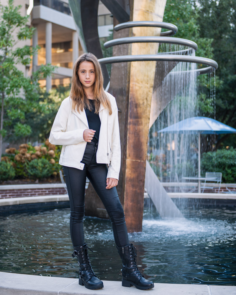 A teenager poses for a portrait in downtown Columbia, SC in front of a fountain.