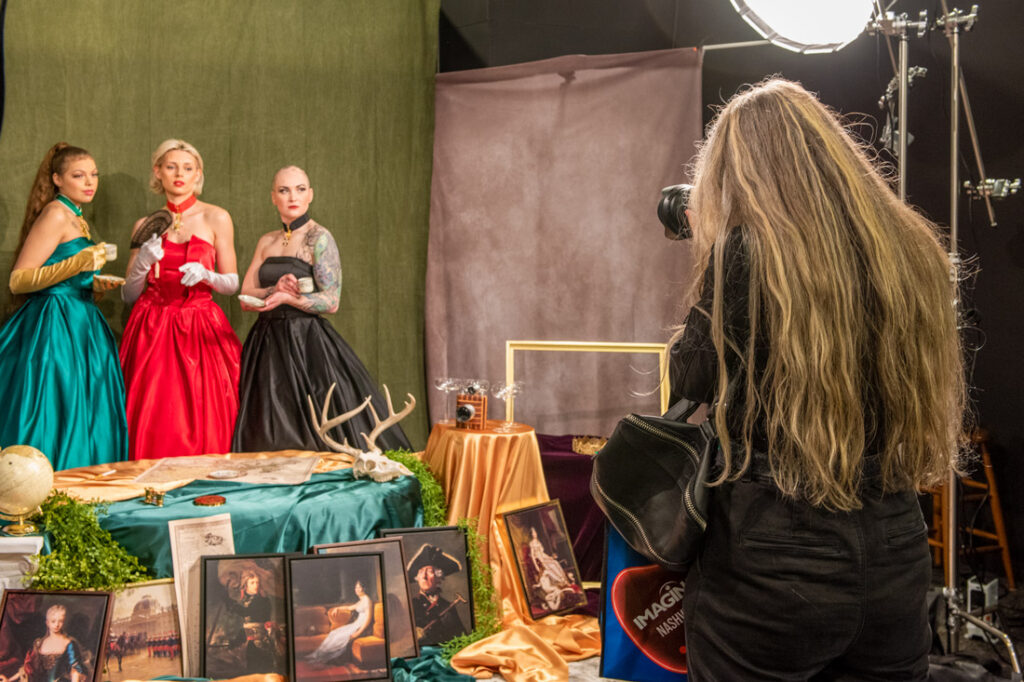 A photographer attending ImagingUSA 2023 photography conference tries lighting by photographing three models at a vendor booth.
