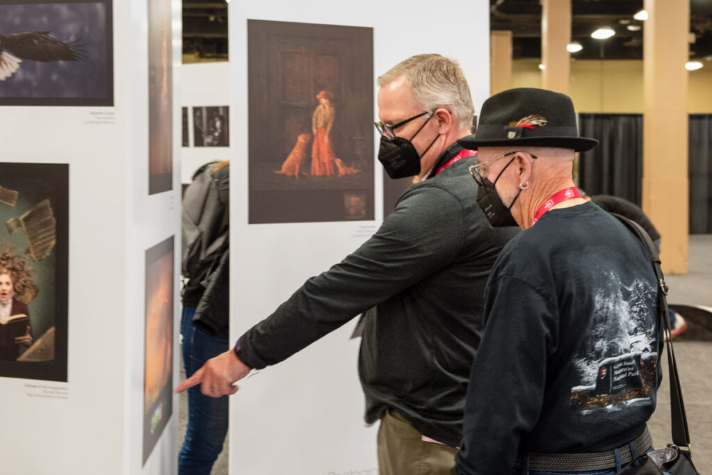 Two people view images from the International Photographic Competition on display at Imaging USA 2023 photography conference.