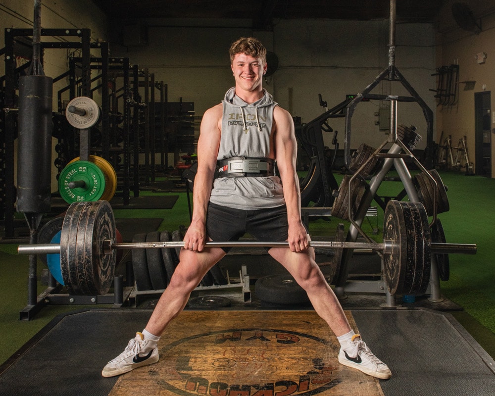 A high school senior graduate poses for a powerlifting portrait at Brickhouse Gym. Senior portraits often feature athletic activities.